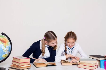 two schoolgirl girls with books and a globe in class at the deskの写真素材