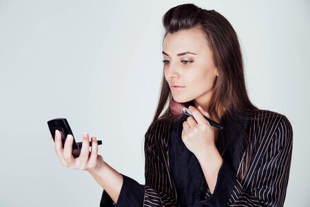 girl in coat makes brush makeup looks in the mirrorの写真素材
