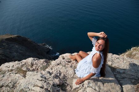 Beautiful woman with long hair in dress on cliff landscape in a journeyの写真素材