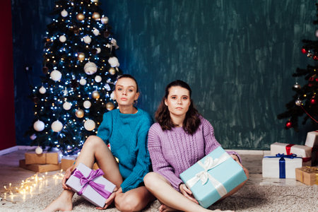 Two beautiful fashionable women at the Christmas tree with gifts for the new year