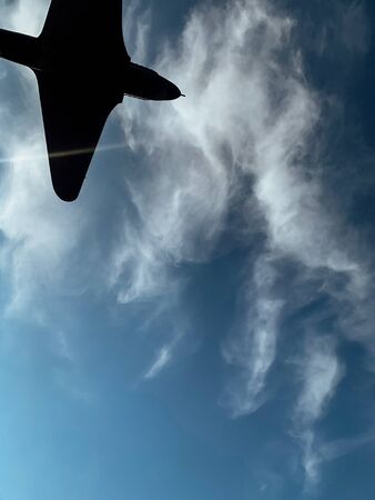 silhouette of an airplane flying in the blue sky with cloudsの写真素材