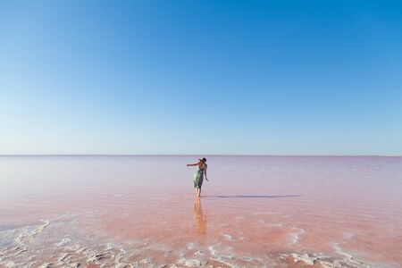 Woman in dress stands in rose water lake against blue skyの写真素材