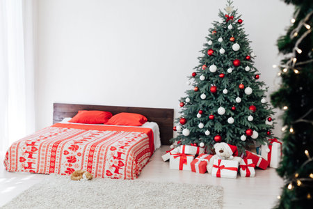 The interior of the white bedroom with a bed with a blue Christmas tree with red gifts for the new...