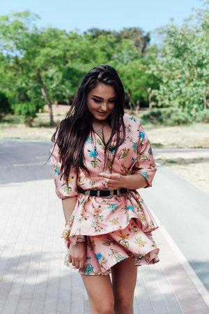 Beautiful fashionable brunette woman in a dress with flowers walks in the park on the street