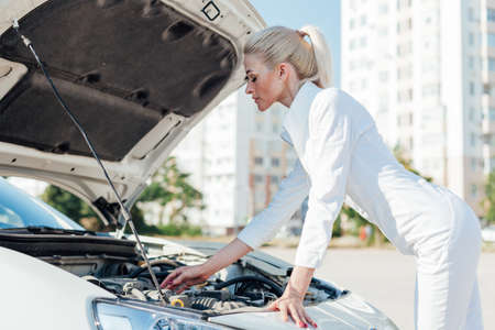 Beautiful female blonde mechanic looks engine under the hood of the carの写真素材