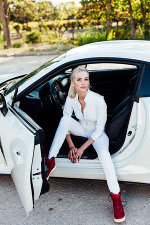 Beautiful female blonde driver behind the wheel of a white carの写真素材