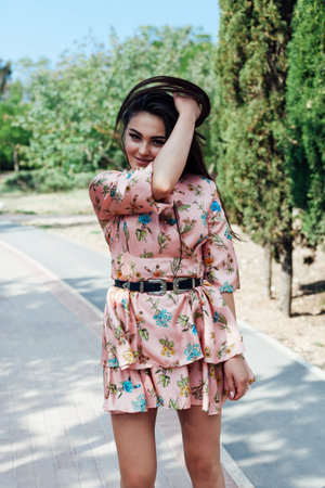 Beautiful fashionable brunette woman in a dress with flowers walks in the park