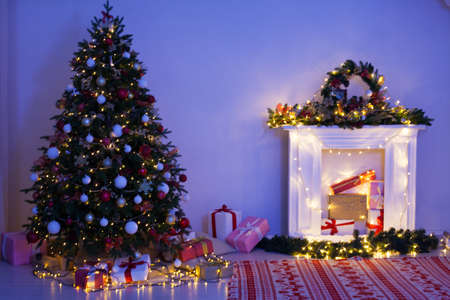 Christmas tree with gifts fireplace lights garlands at night on New Years Eve in the interior of the roomの写真素材