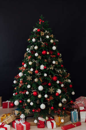 Christmas tree decorated with toys with gifts in the interior of the room black background new yearの写真素材