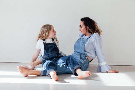 Mom brunette and daughter blonde in jeans sit on the floorの写真素材