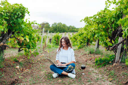 Beautiful woman in white dress with laptop work online with a glass of wineの写真素材