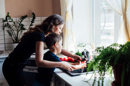 Mom and young son wash fresh vegetables in the kitchenの写真素材