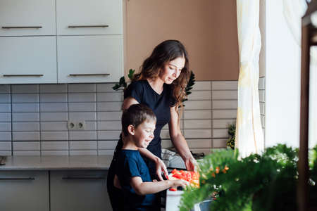 Mom and young son cut fresh vegetables to make salad in the kitchenの写真素材
