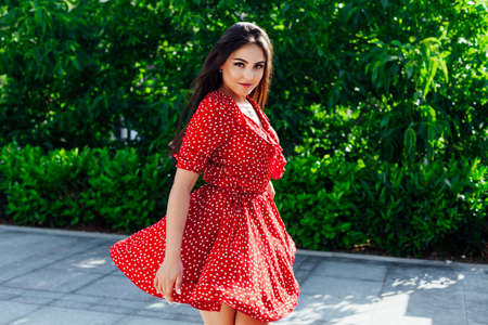 Beautiful brunette woman in red dress in polka dots walks in the streetの写真素材