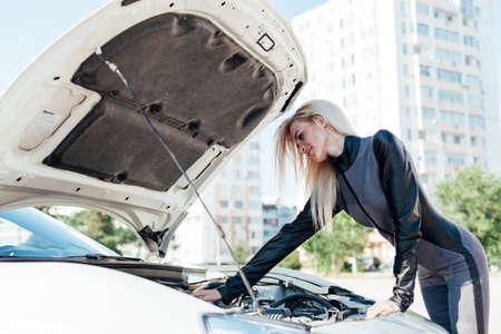 Beautiful blonde woman on the road repairs the engine of a white carの写真素材