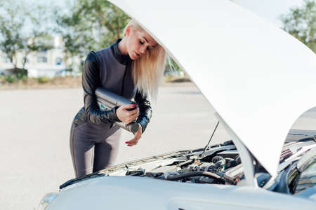Beautiful blonde woman on the road repairs the engine of a white carの写真素材