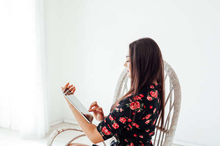 Beautiful fashionable woman in a chair with an internet tabletの写真素材