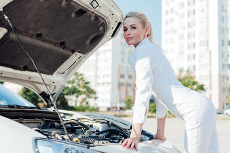 Beautiful female blonde driver repairs motor under car hoodの写真素材