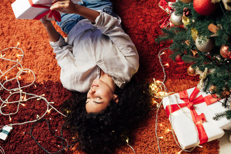 Beautiful brunette woman lies at the Christmas tree with lights garlands new yearの写真素材