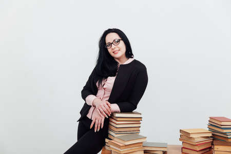 Beautiful female teacher in class at a table with stacks of educational booksの写真素材