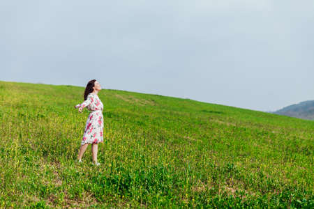 Beautiful brunette woman in a dress with flowers stands on the mountain oneの写真素材