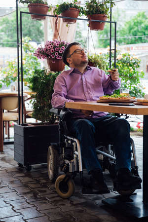 Disabled man with wheelchair in restaurant eats pizzaの写真素材