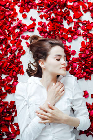 beautiful woman lies among the red petals of rose flowersの写真素材