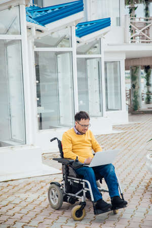 a man with disabilities in a wheelchair works at a computer on the Internetの写真素材