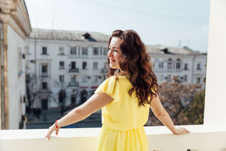 portrait of a beautiful brunette woman in a yellow dress at homeの写真素材