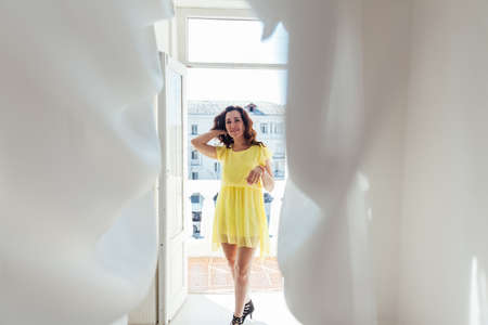 portrait of a beautiful brunette woman in a yellow dress at homeの写真素材
