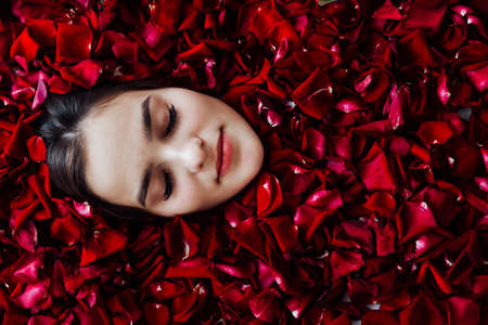 beautiful face of a woman in red rose petalsの写真素材
