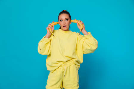 beautiful woman plugged ears yellow banana on blue backgroundの写真素材