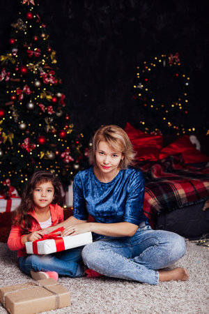 mother and daughter opens gifts at the Christmas tree for the new yearの写真素材
