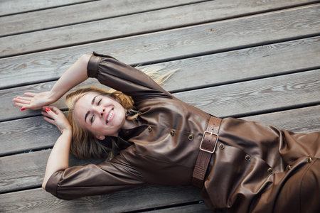 beautiful blonde woman in a raincoat on a wooden benchの写真素材