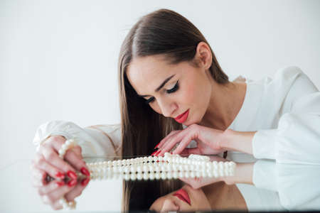 portrait of a beautiful brunette woman at the mirror with pearl beadsの写真素材