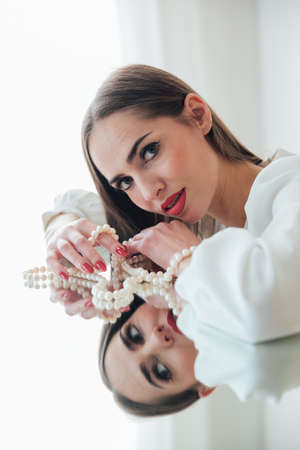 portrait of a beautiful brunette woman at the mirror with pearl beadsの写真素材