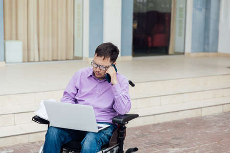a man with disabilities in a wheelchair works on a laptop in the Internetの写真素材