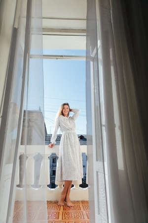 beautiful blonde woman in a dress on the balcony looks at the streetの写真素材