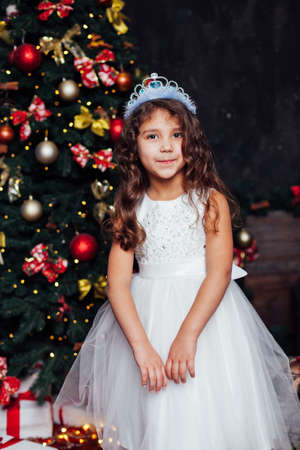 little girl 5 years old in a white dress princess at the Christmas treeの写真素材