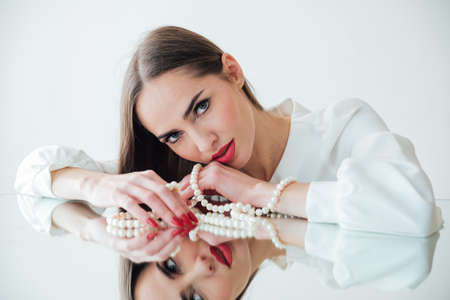 portrait of a beautiful brunette woman at the mirror with pearl beadsの写真素材