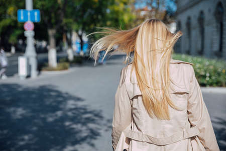 a beautiful blonde woman in an autumn raincoat walks outsideの写真素材