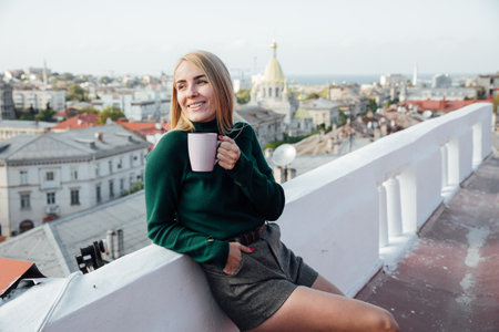beautiful blonde woman on the roof of the attic looks at the cityの写真素材