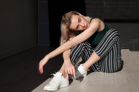 beautiful fashionable blonde woman in green clothes sit on floor