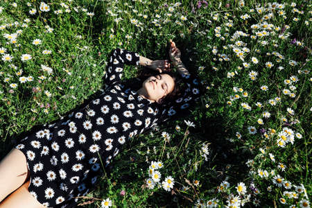 beautiful woman in lies in the grass with chamomile flowersの写真素材