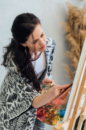 beautiful woman artist paints a picture with paints on an easelの写真素材