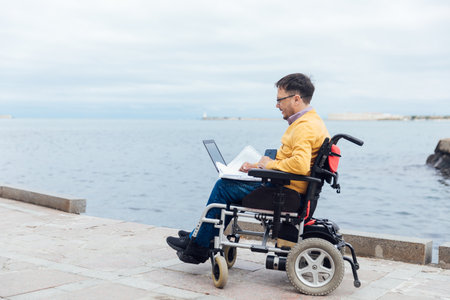 A man with disabilities sits with a laptop by the seaの写真素材