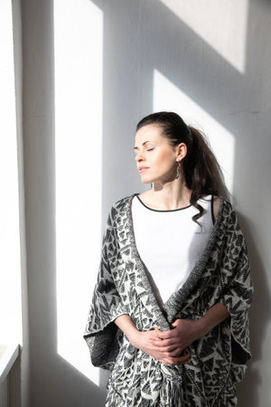 a woman stands on a white background in the shade from the windowの写真素材