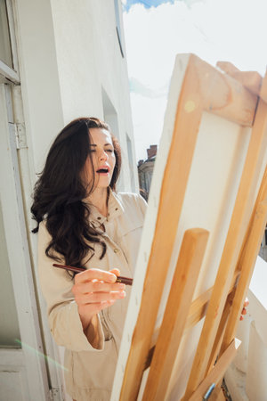 a female artist stands at an easel on a balcony