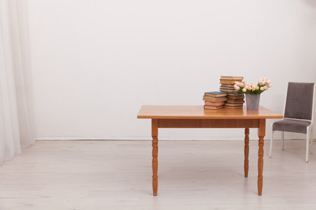 cabinet table with a stack of books and a vase of flowers chair by the tableの写真素材