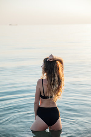a woman in a black swimsuit stands in the water in the sea rest on the beachの写真素材